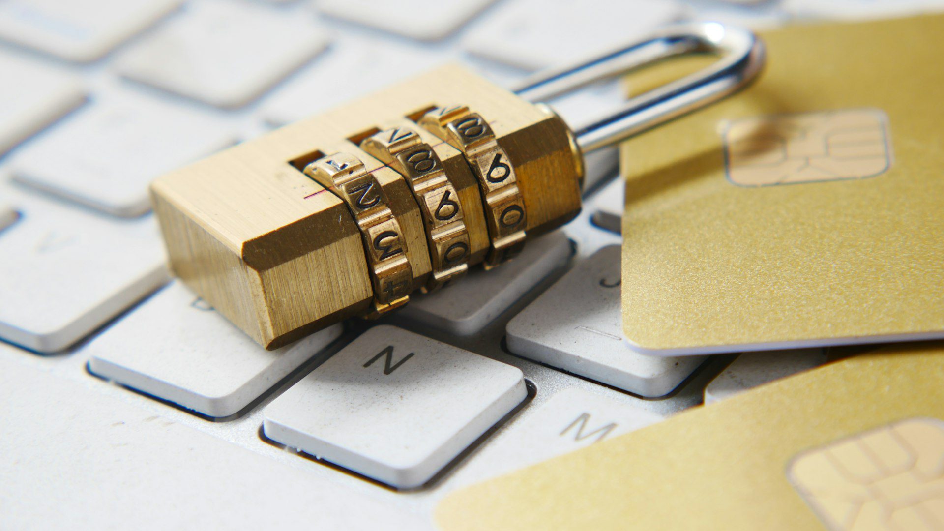 Brass combination padlock resting on a computer keyboard beside credit cards, symbolizing website SSL security