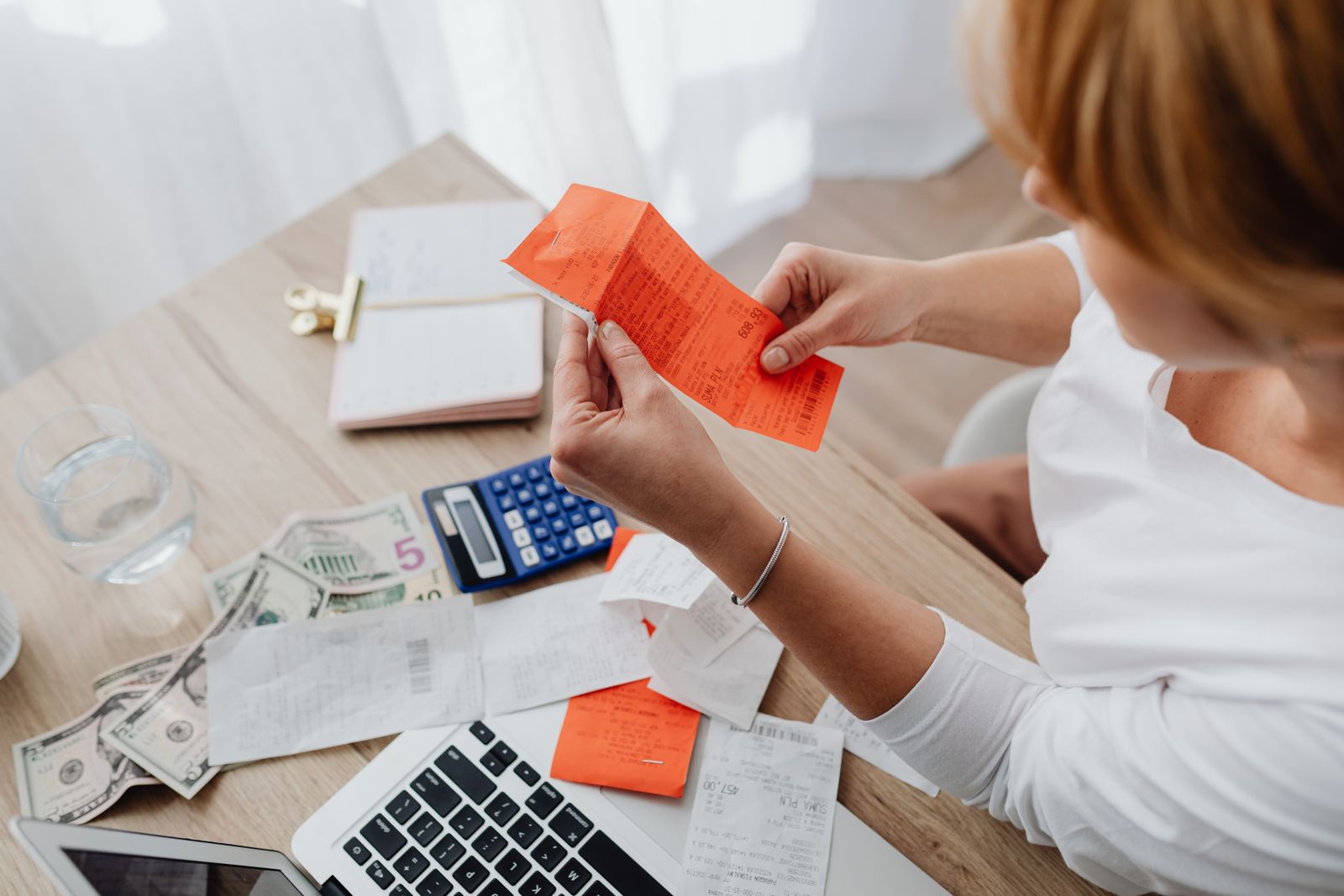 Small business owner reviewing receipts with a calculator and laptop to plan a budget