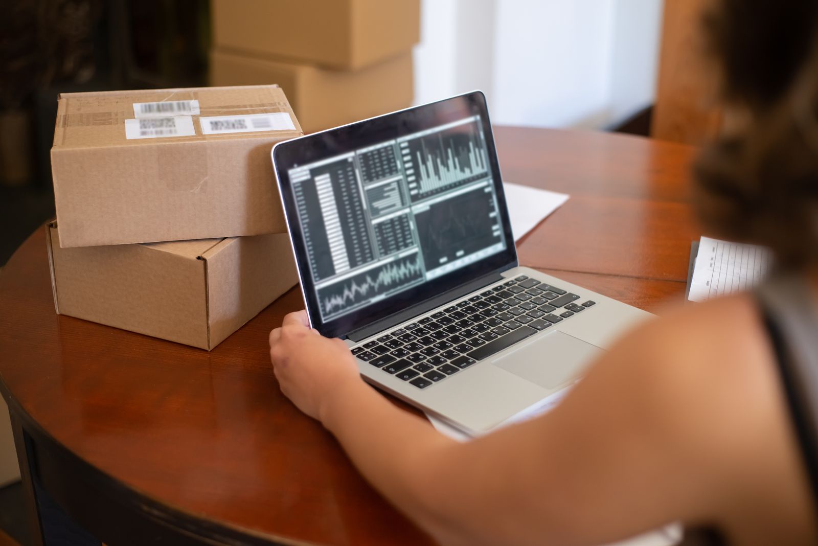 Small business owner at a laptop beside shipping boxes, checking for new website leads